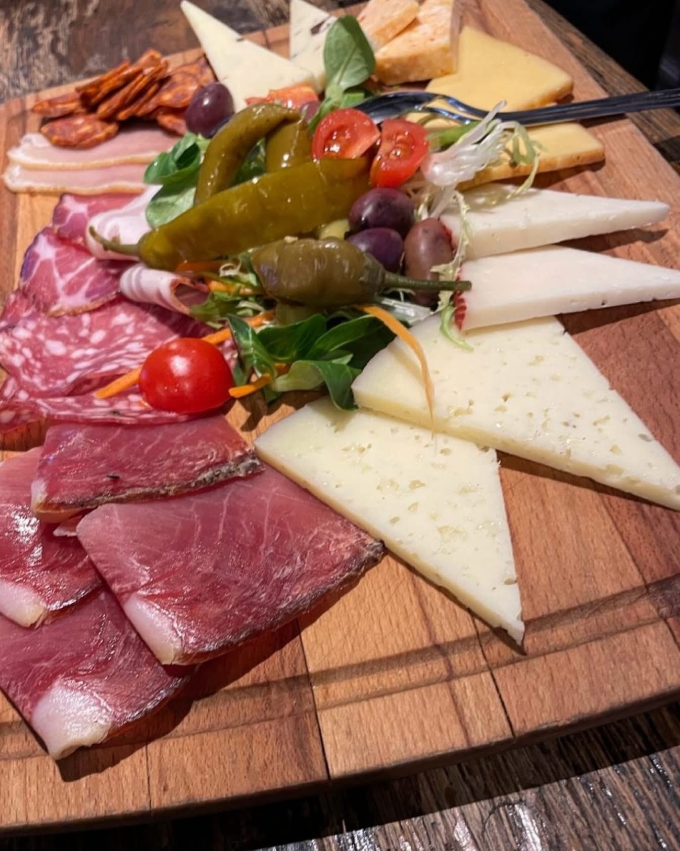 Wooden charcuterie board with cheeses, cured meats, peppers and tomatoes